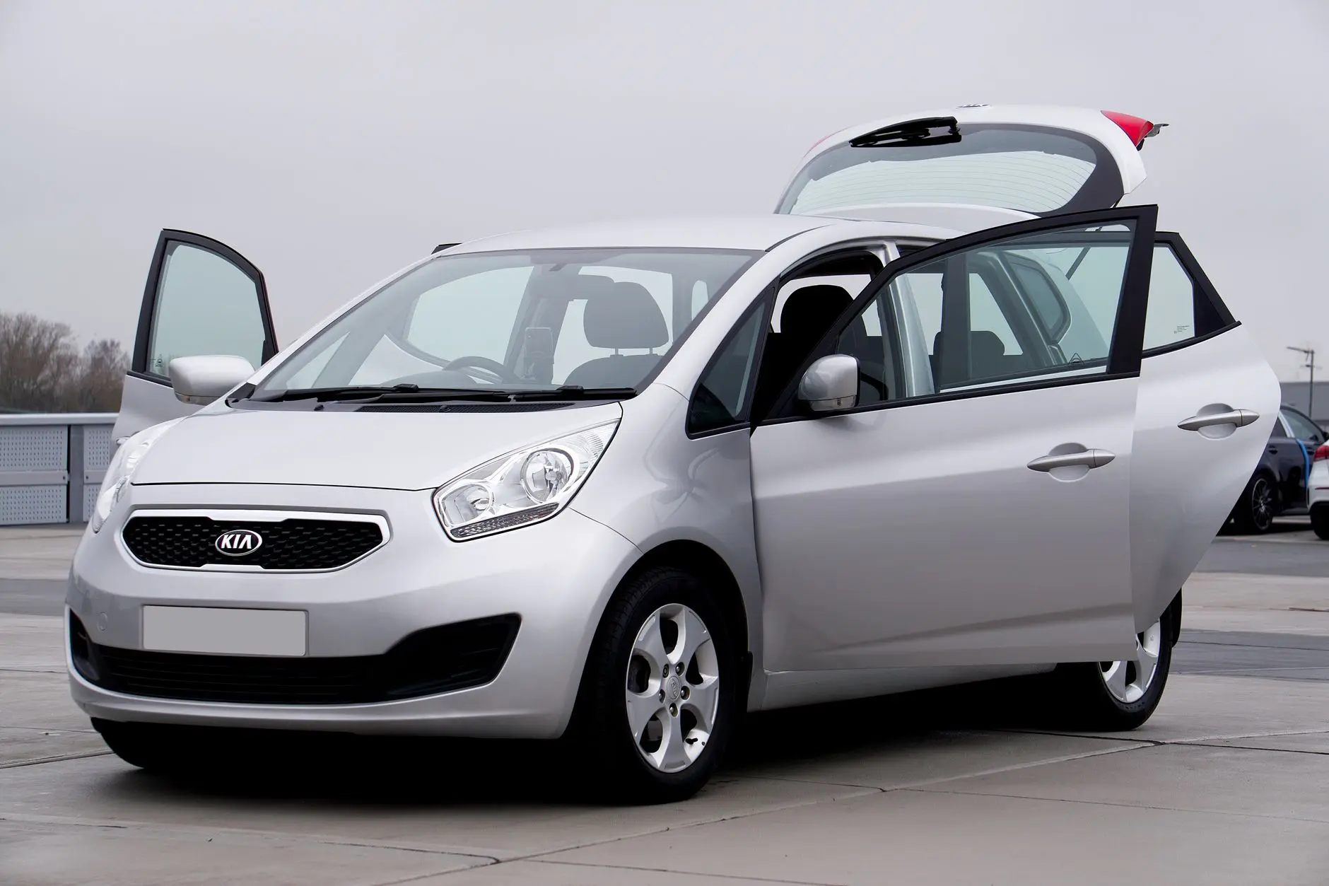 Silver Kia hatchback car photographed with doors open, parked outdoors on a cloudy day.