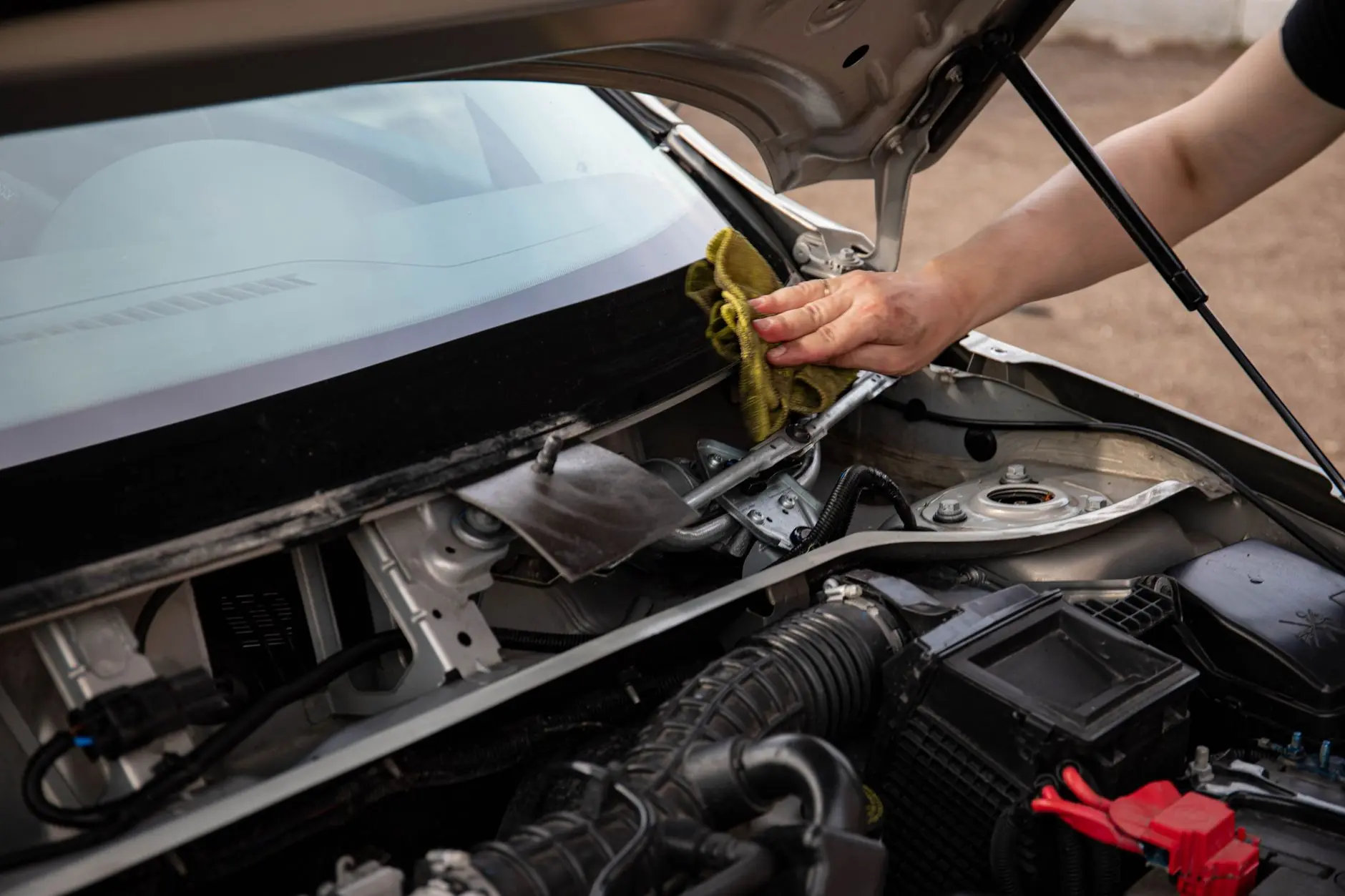 A mechanic wipes the windshield of a car, focusing on engine and windshield maintenance.