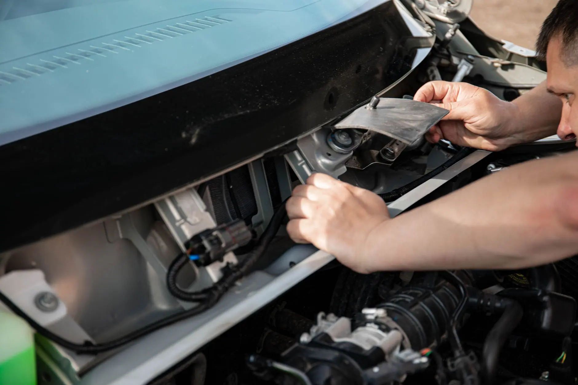 Close-up of a mechanic working on a car engine outdoors in bright daylight.